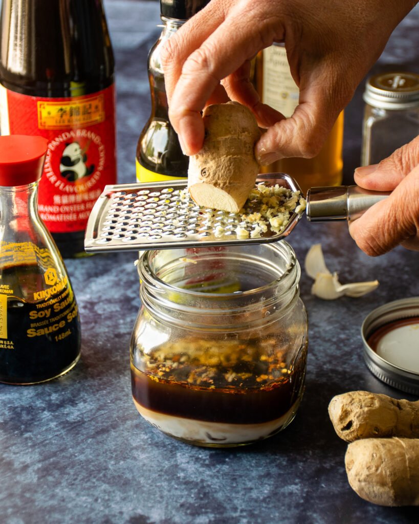 A hand grating fresh ginger into a mason jar with other ingredients. 