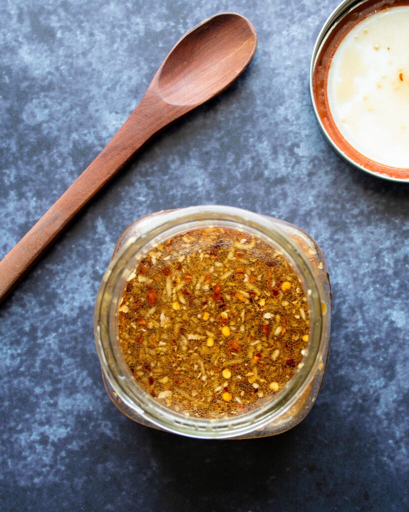 Looking down on a jar of stir fry sauce with a wooden spoon and an open lid next to it.