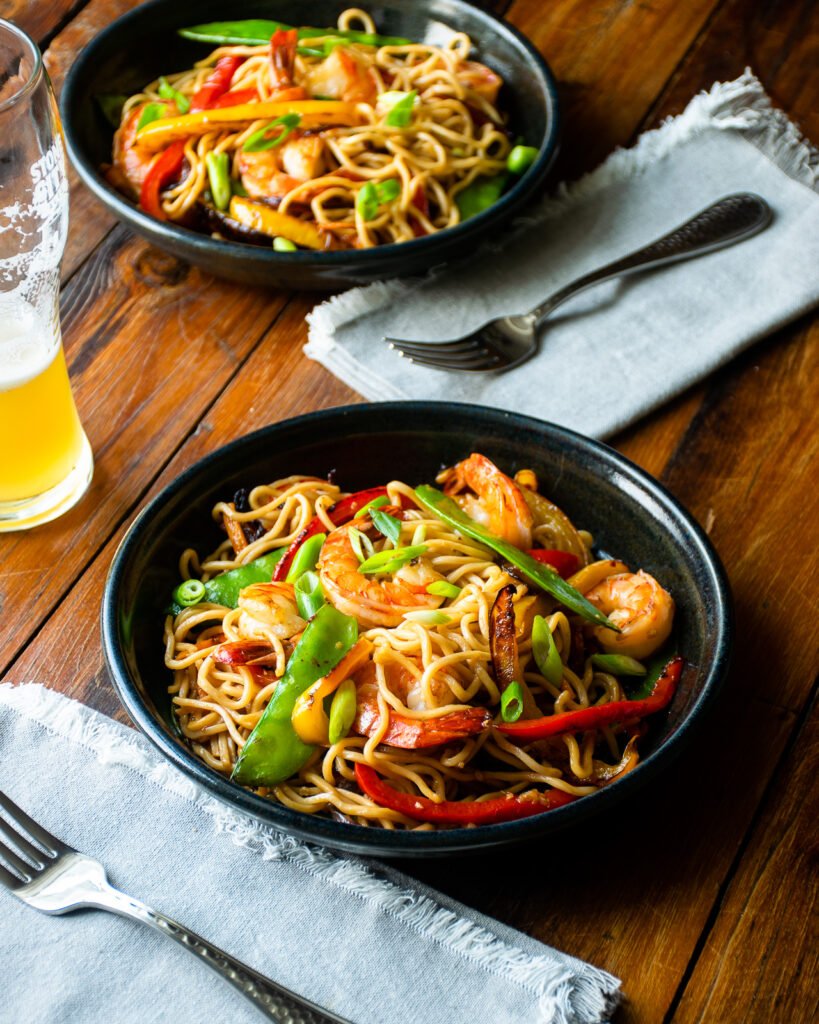 Two bowls of shrimp stir fry on a wooden table.