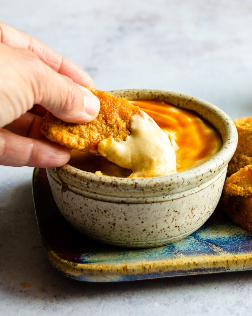 A hand dipping an apple fry into caramel cream dip.