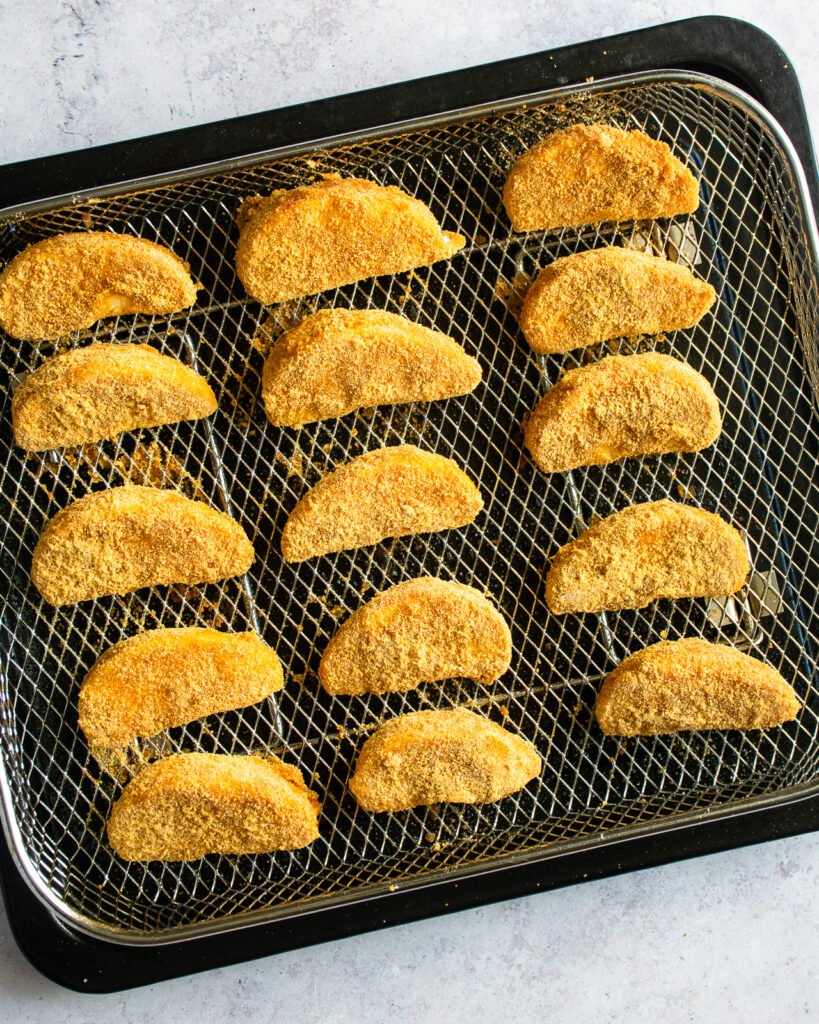 Breaded apple wedges on a air frying basket with tray underneath.