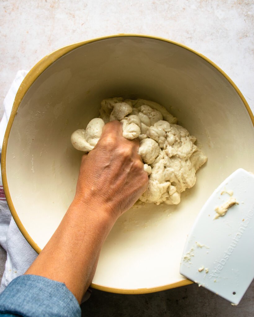 A hand squeezing dough in a large bowl.