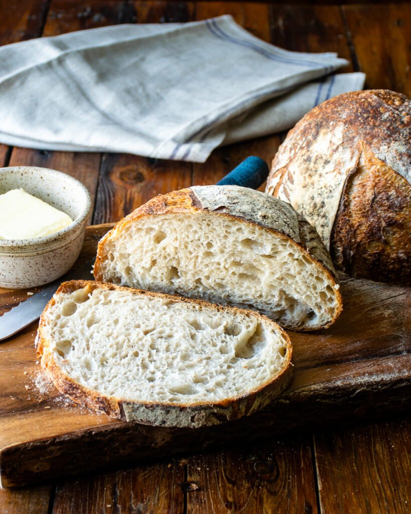 A loaf of sourdough bread sliced open on a cutting board with a dish of butter next to it.
