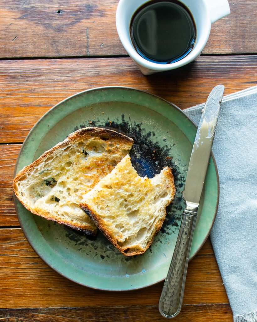 A plate of toast with a bite taken out of it with a knife and a cup of coffee.