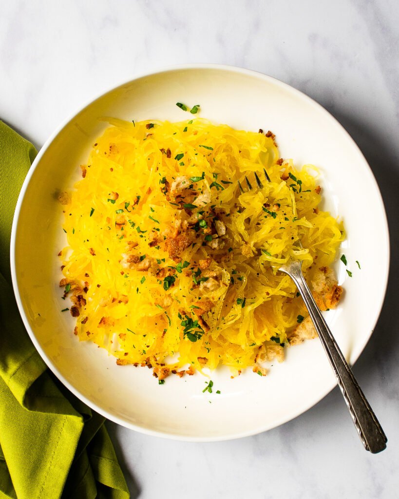 Spaghetti Squash with breadcrumbs and a fork and a green napkin on a marble countertop.