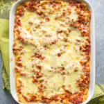 An overhead shot of lasagna with zucchini in a casserole dish with a green towel.