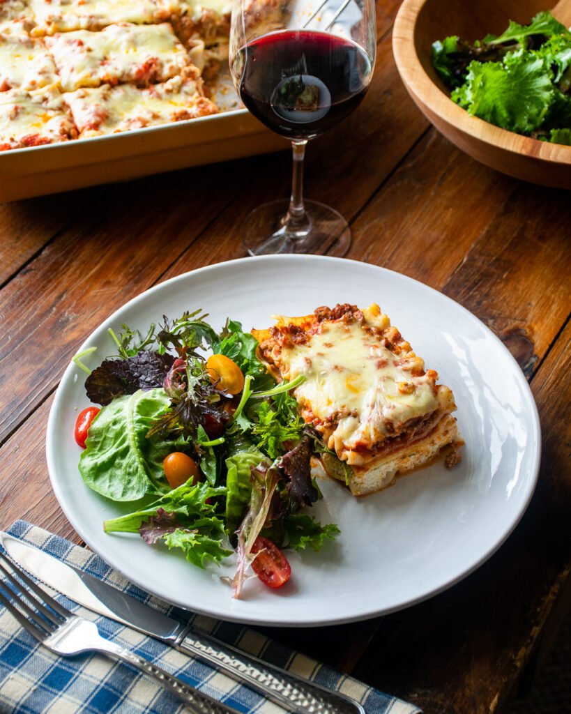 A piece of lasagna with zucchini on a white plate with a side of salad greens.
