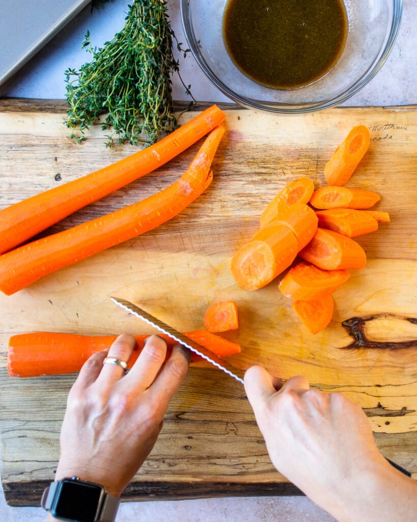 Hands cutting carrots into large diagonal slices.