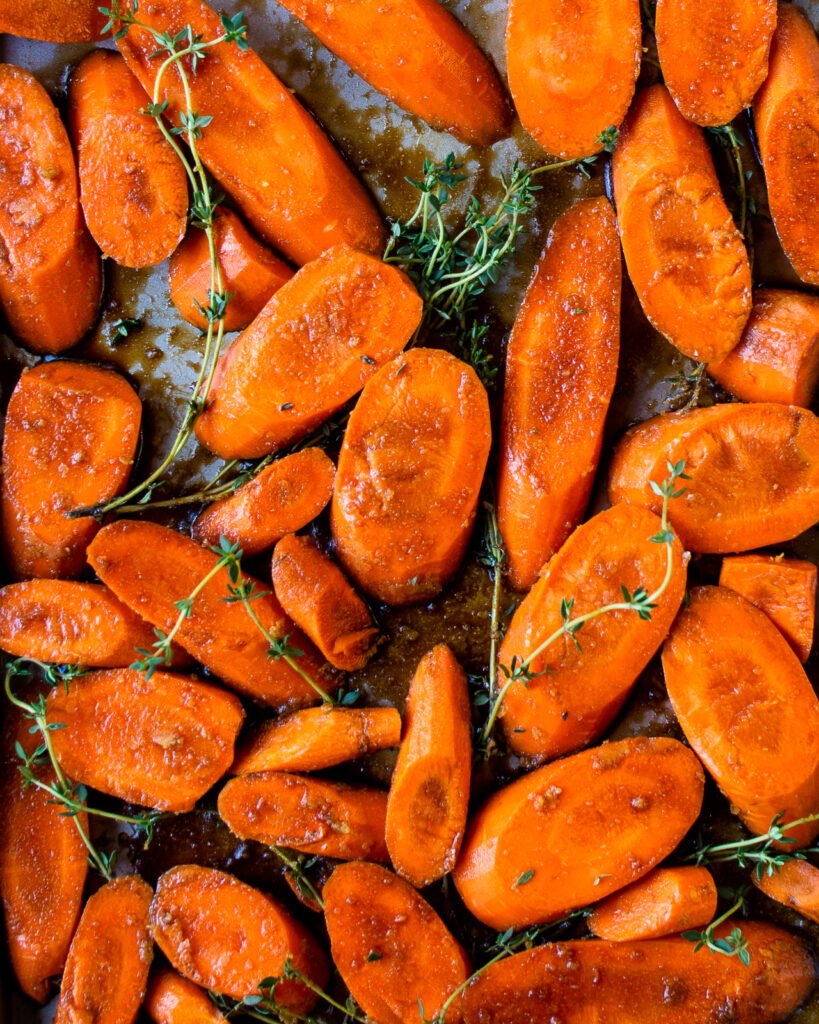 Raw carrots and thyme with balsamic vinegar glaze on a baking sheet.