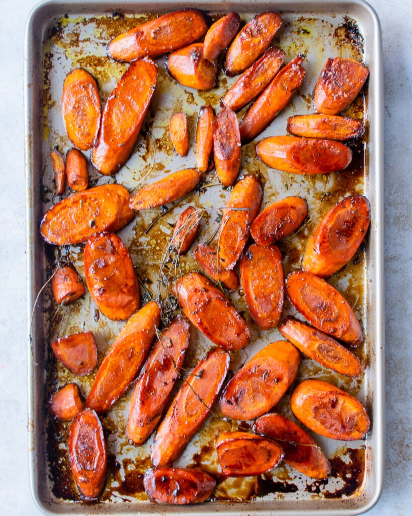 Cooked carrots and thyme with balsamic vinegar glaze on a baking sheet.