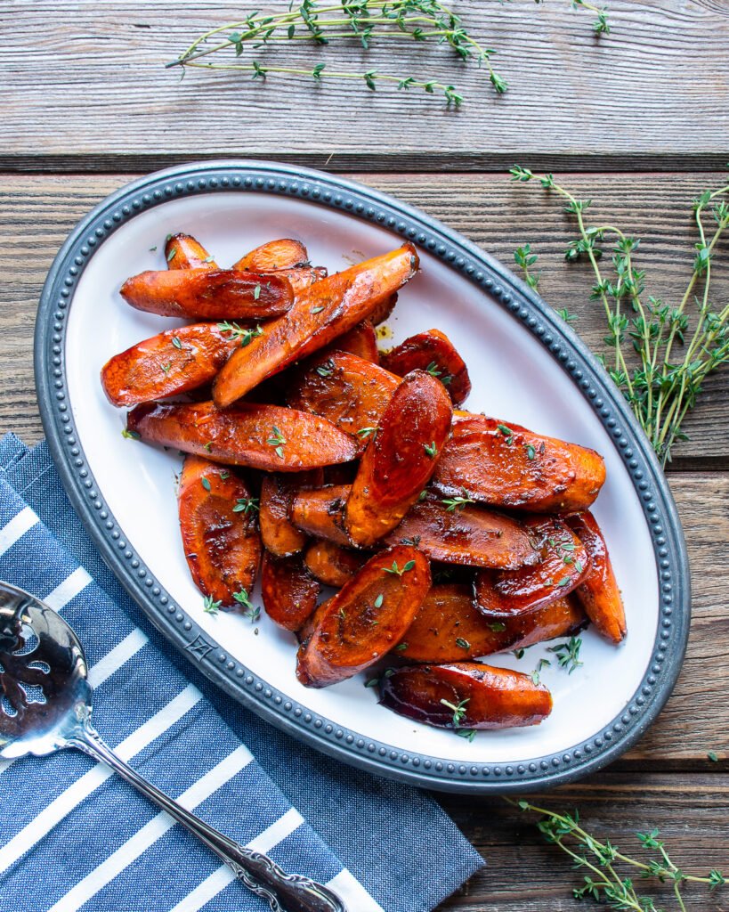 Balsamic Glazed Carrots on an oval white plate with a blue napkin and serving spoon.