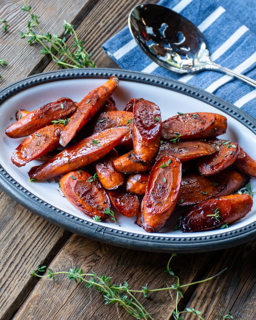 Balsamic Glazed Carrots on an oval white plate with a blue napkin and serving spoon.