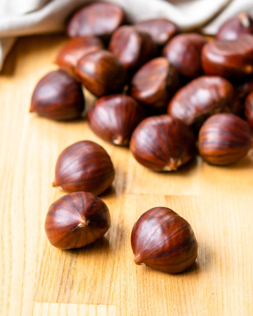 Chestnuts on a butcher block with a kitchen towel in the background.
