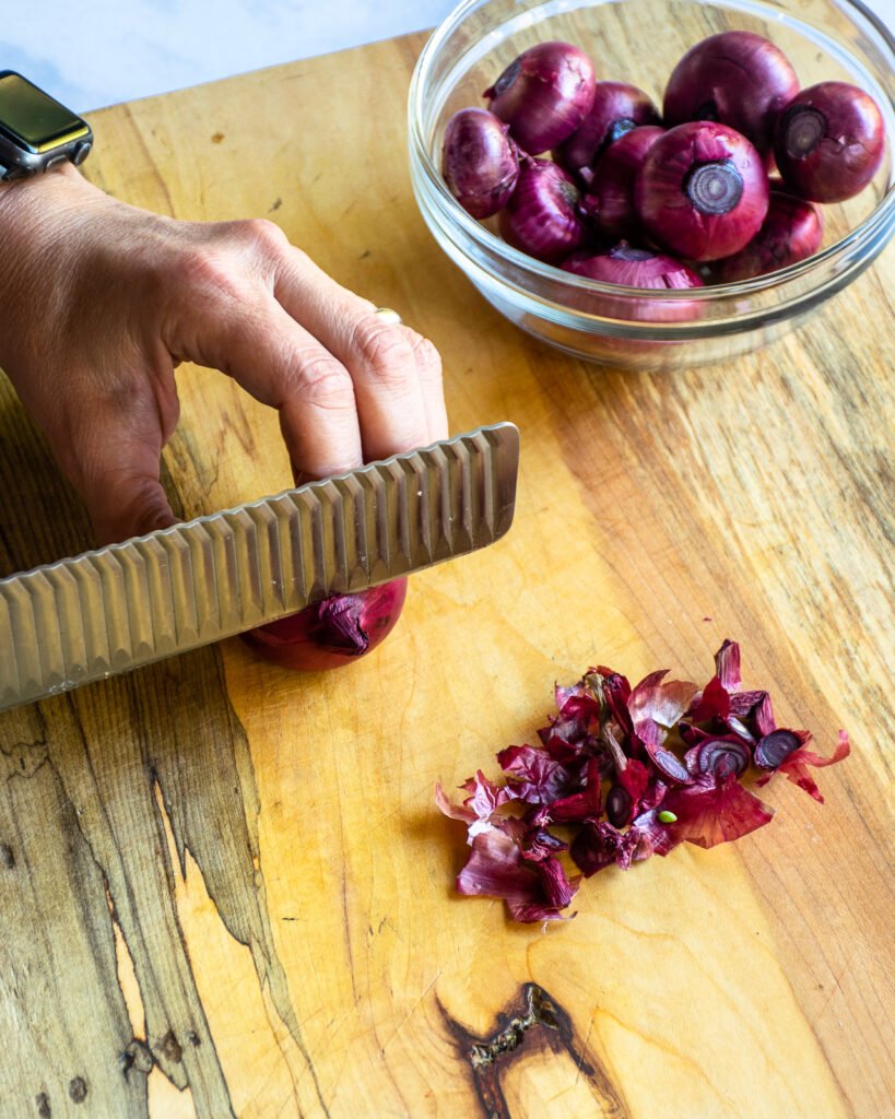 Hands cutting the tip off a red cipollini onion.
