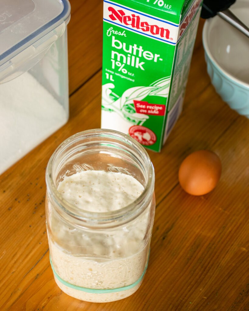 Sourdough starter, an egg and some buttermilk on a wooden table.