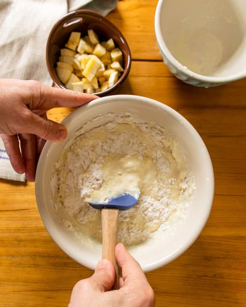 Hands stirring a batter together with a small bowl of chopped banana near by.