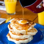 Sourdough buttermilk banana pancakes on a blue plate with syrup being poured over the top.
