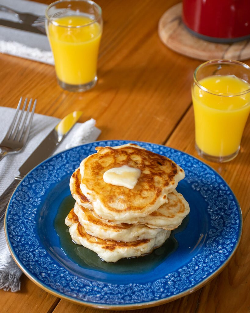 Sourdough Buttermilk pancakes on a blue plate with glasses of orange juice and place settings on a table.