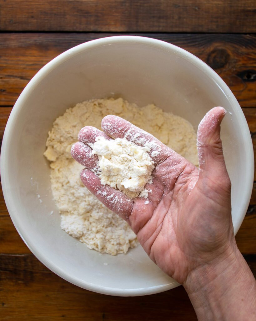 A hand showing chunks of butter in a bowl of flour.