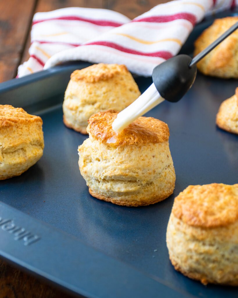 A basting brush brushing butter on top of baked sourdough buttermilk biscuits.