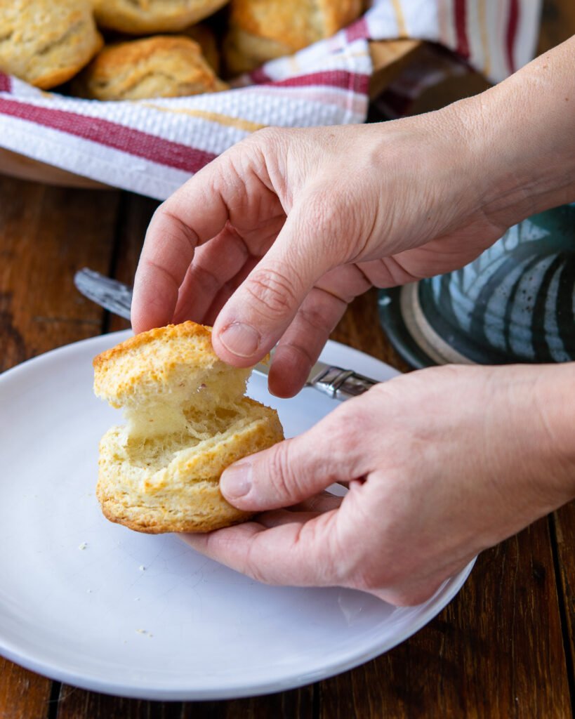 Hands pulling a biscuit apart over a white plate.