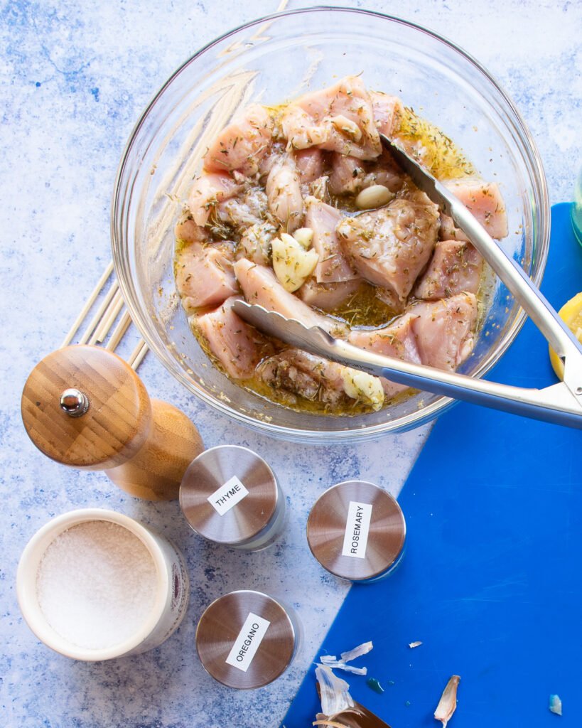 Chicken souvlaki marinating in a glass bowl.