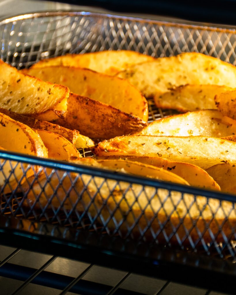 Greek Potato Wedges cooking in the basket of an air fryer oven.