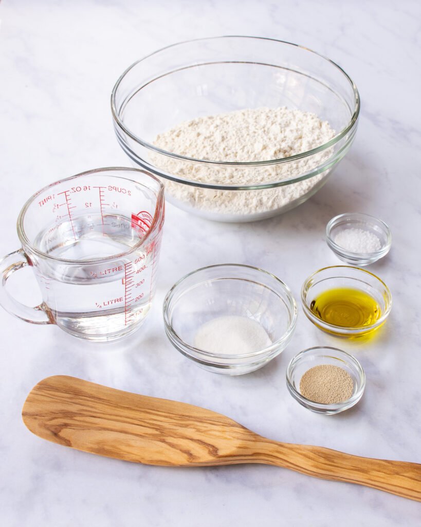 Ingredients in glass bowls on a marble countertop with a wooden spoon.