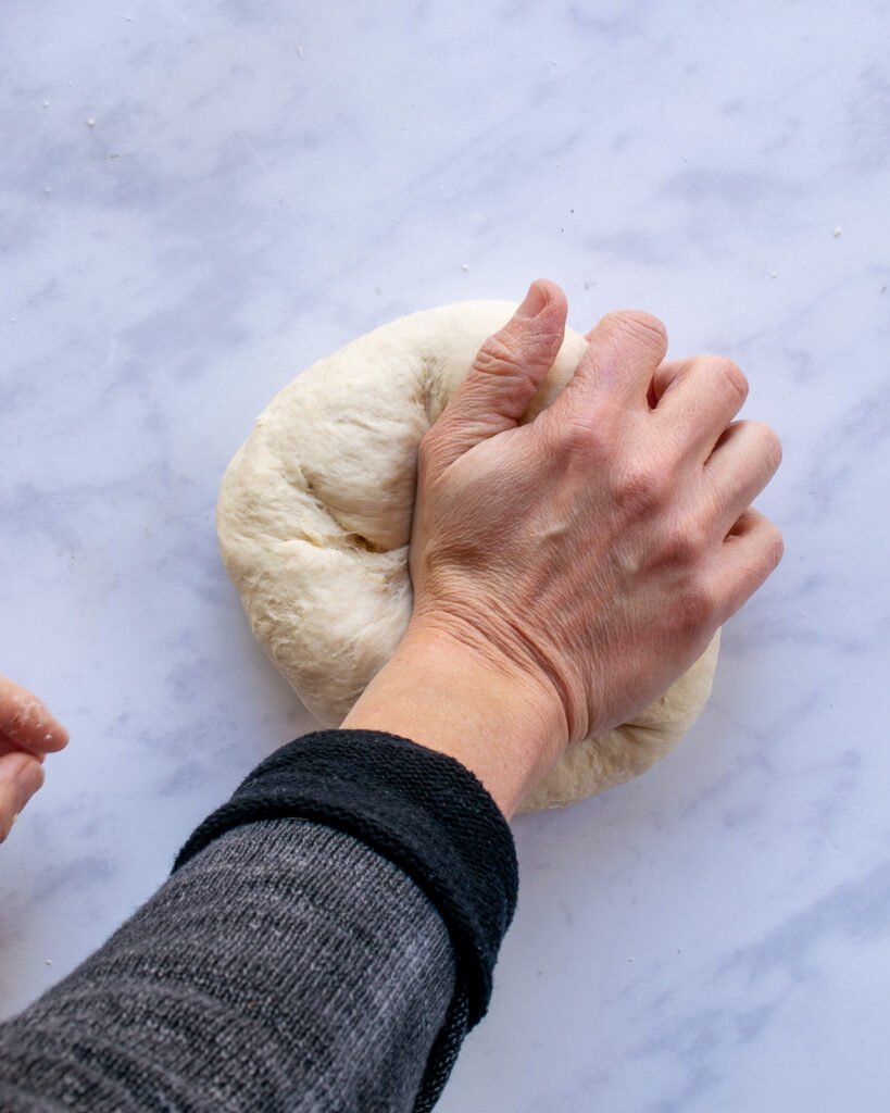 A hand kneading dough on a marble countertop.