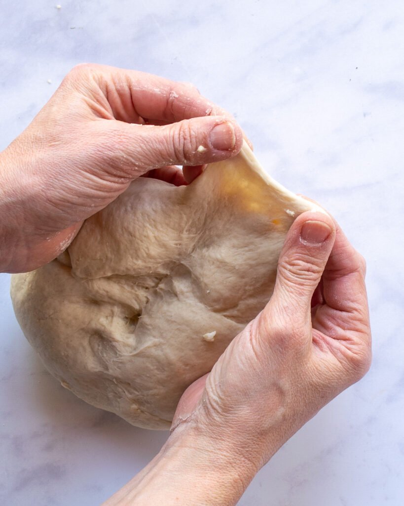 Fingers stretching dough away from a ball to show its elasticity.