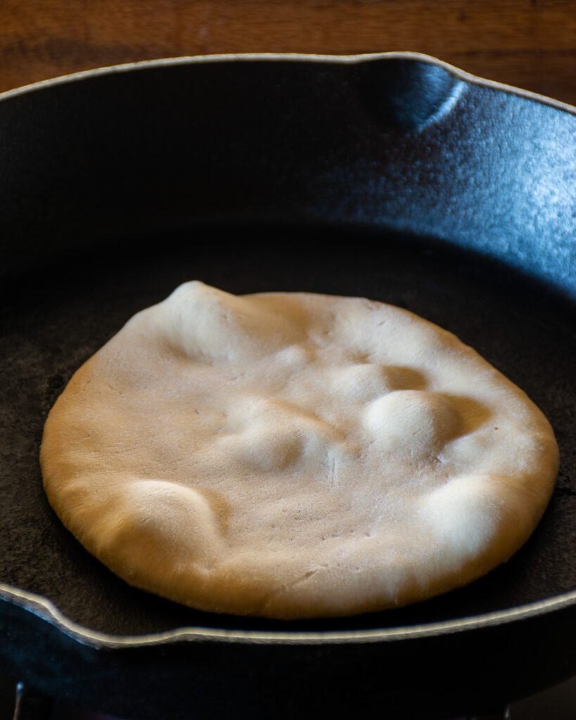 Pita bread cooking in a cast iron skillet.