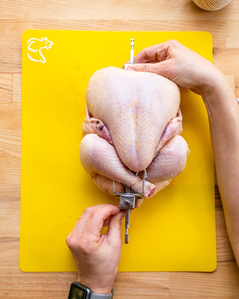 Two hands placing a trussed chicken on a rotisserie spit.