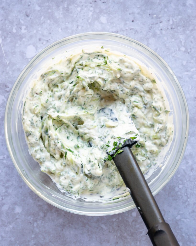 A bowl with tzatziki sauce mixed in it with a black spatula.