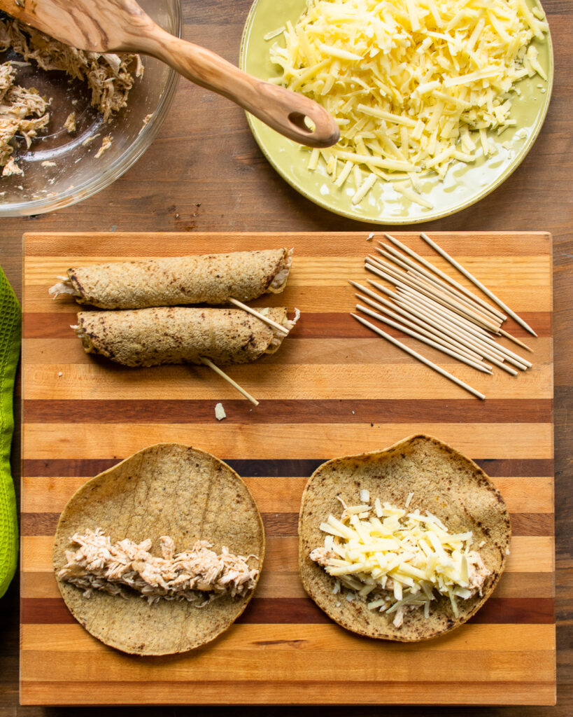 Chicken and green chili taquitos being built on a wooden cutting board.