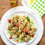 Chicken and green chili taquitos on a white plate with a green checkered napkin and a bottle of beer.