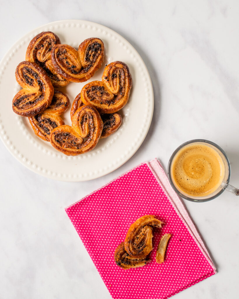 Chocolate Palmiers on a white plate with one palmier on a pink beverage napkin with an espresso.