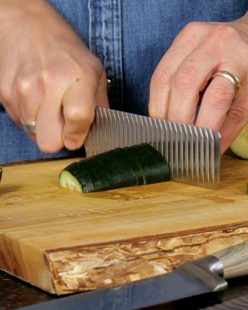 A nakiri knife cutting through zucchini on a wooden cutting board.