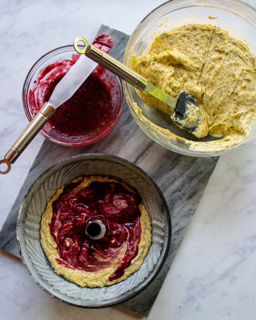 Building a lemon blackberry poppy seed bundt cake with layers of cake batter and blackberry purée.