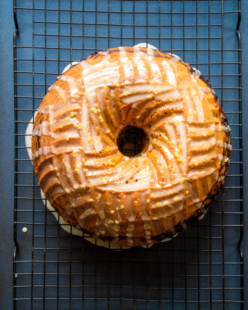 Glazed lemon blackberry poppy seed bundt cake on a rack over a blue sheet pan.