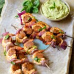 Grilled shrimp chorizo skewers on a large rectangular platter with a dish of green dip.