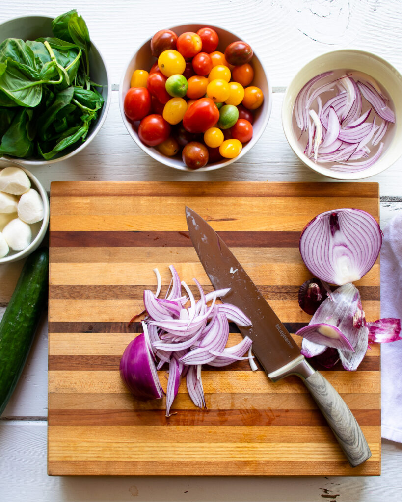 Red onions being cut on a wooden cutting board with other ingredients around.