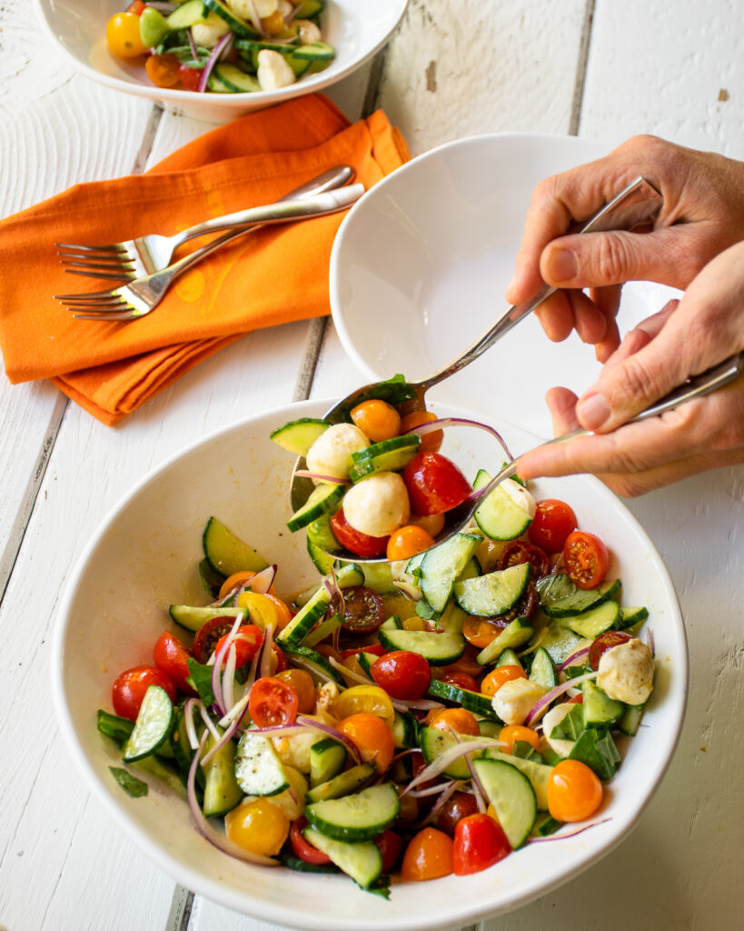 Tomato Cucumber Salad in a white bowl on a white wooden table with orange napkins.