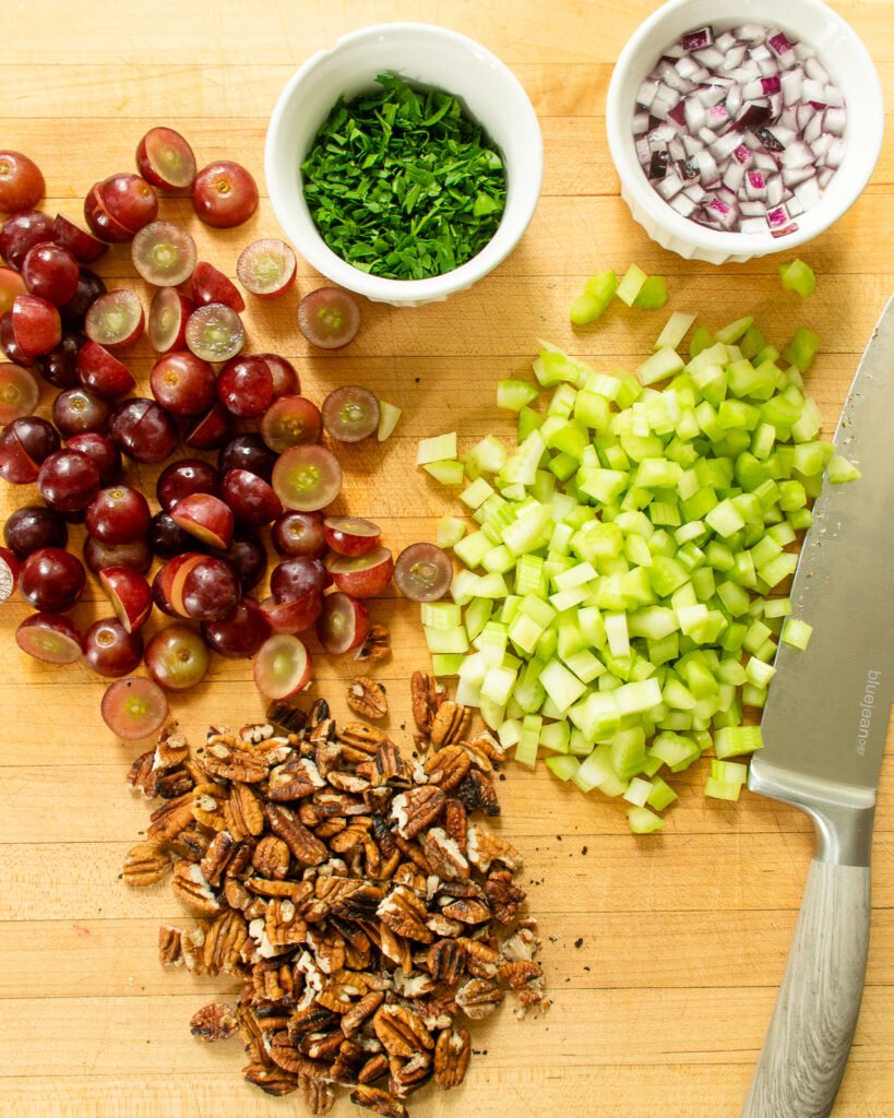Ingredients chopped on a cutting board - grapes, pecans, celery, parsley and red onion.