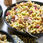 Chicken macaroni salad in a dark bowl on a countertop with a serving spoon..