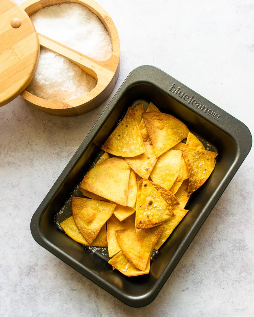 Air fryer tortilla chips in a baking pan with salt next to it.