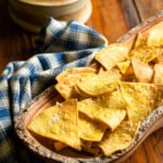 Air fryer tortilla chips in a wooden bowl with a bowl of salsa in the background.