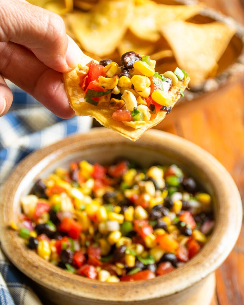 A hand dipping a tortilla chip into corn and black bean salsa.