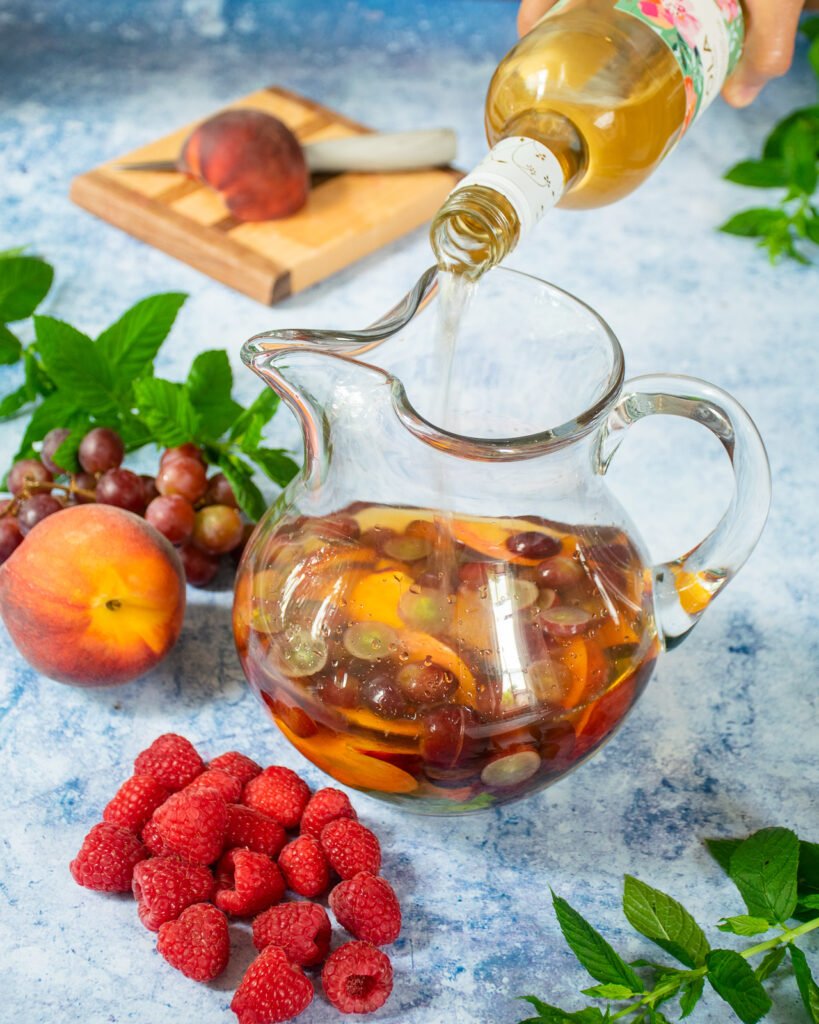 Pouring wine into a glass pitcher with fruit inside.