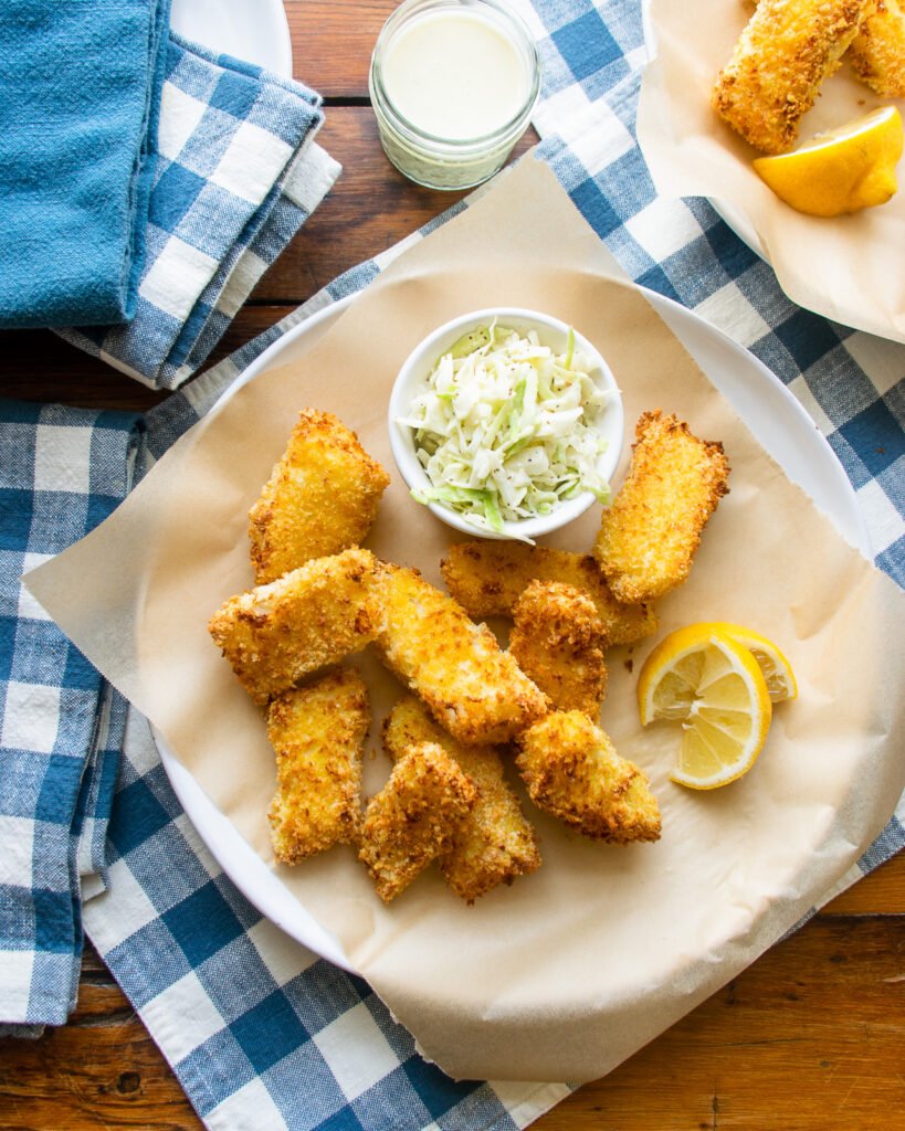Air fryer fish sticks on a parchment lined plate with coleslaw and a lemon wedge.