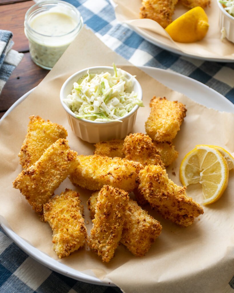 Air fryer fish sticks on a parchment lined plate with coleslaw and a lemon wedge.